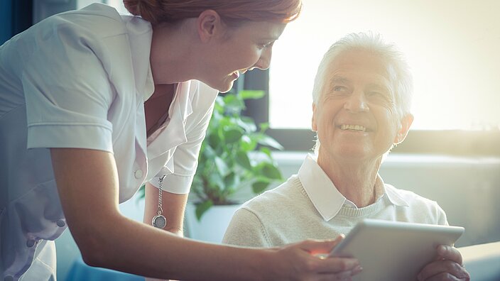 Eine Krankenschwester zeigt einem älteren Mann berichte auf einem Tablet-PC